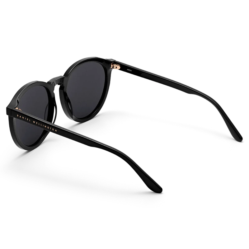 Minimalist Daniel Wellington Arch sunglasses in black bio-acetate with dark lenses and elegant gold-tone branding.