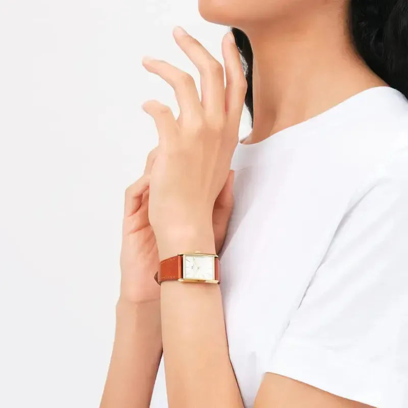 Daniel Wellington Bound gold watch with a white rectangular dial and light brown crocodile leather strap on a wrist.