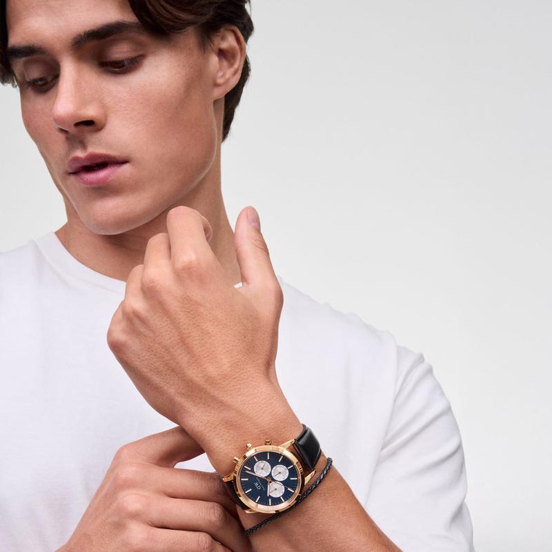 Daniel Wellington braided black leather bracelet with gold-tone hardware worn alongside a matching gold chronograph watch.
