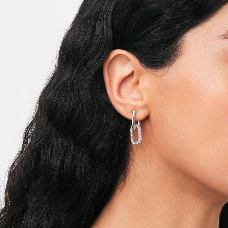 Chunky silver link earrings featuring refined crystal details on a polished brass base worn on an earlobe.