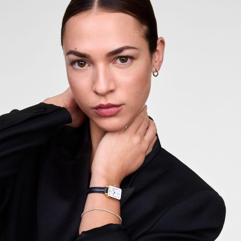 Elegant gold Daniel Wellington Quadro watch with a sleek black leather strap and textured dial on a model.