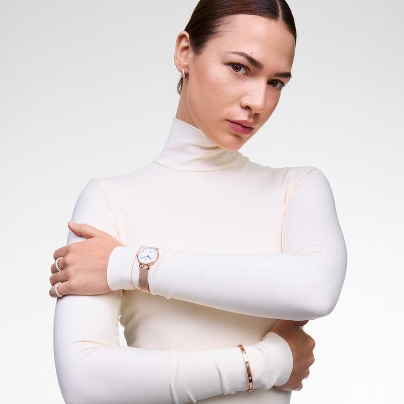 Elegant 28mm rose gold Daniel Wellington watch with a mesh strap and Roman numeral dial worn by a woman.