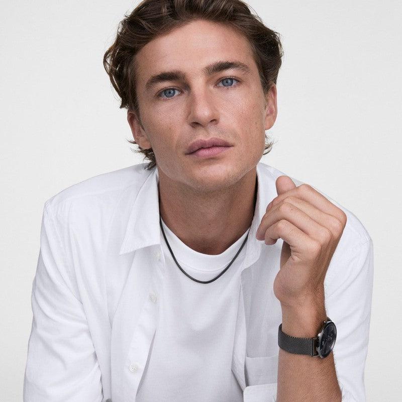 Unisex Daniel Wellington Tide mesh necklace in graphite stainless steel worn by a man in a white shirt.