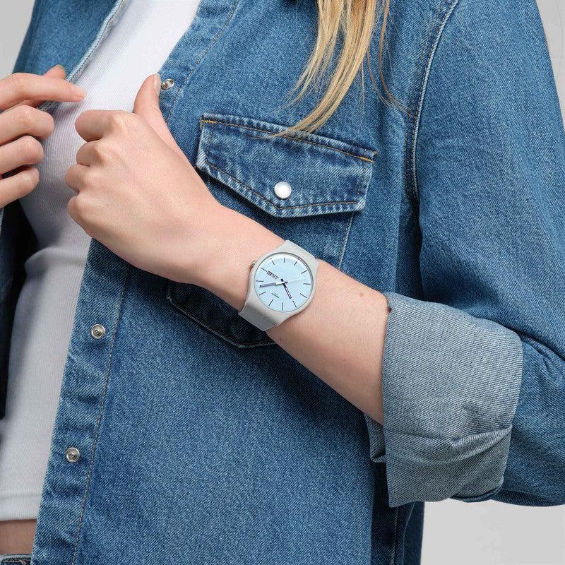 Swatch Blueberry Sky watch featuring a light blue dial, grey biosourced case, and matching silicone strap on a wrist.