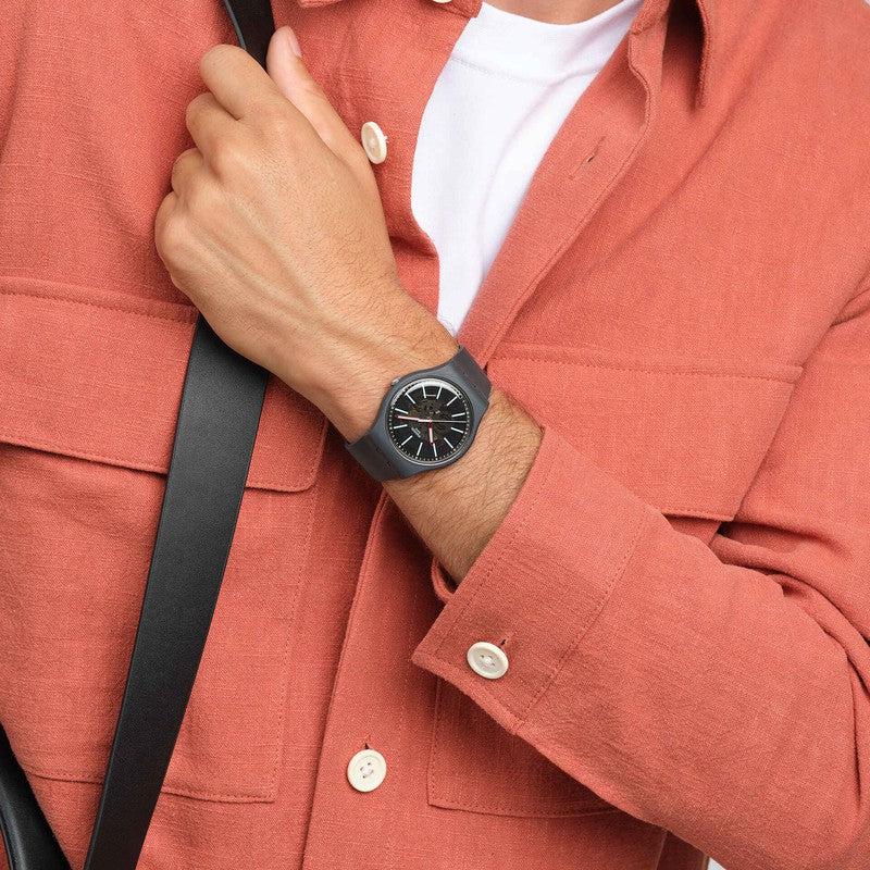 Swatch Coblestone Street watch with a dark gray biosourced case, transparent dial, and light blue accents worn on a wrist.