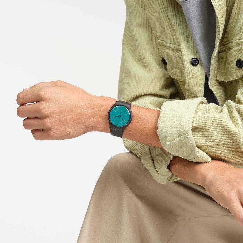 Swatch Dark Duality watch with a shimmery green mirror dial and brown biosourced case worn on a wrist.