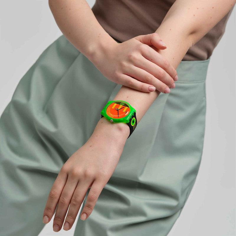 Swatch Neon Rider watch featuring a vibrant neon yellow dial, green biosourced case, and black patterned silicone strap on a wrist.