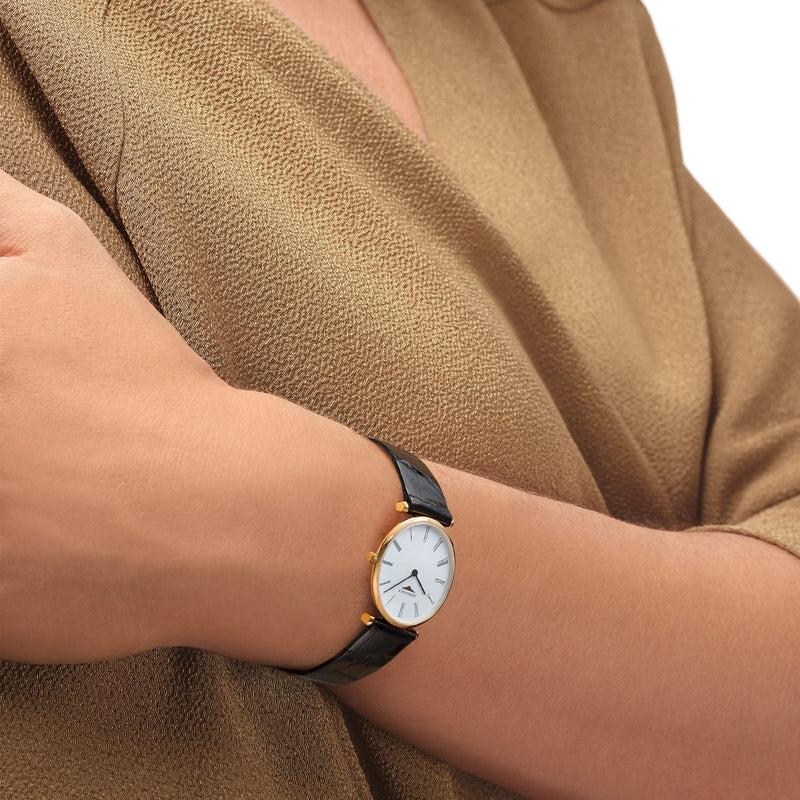 Elegant Longines La Grande Classique watch with a 29mm yellow PVD case, white dial, and black leather strap on a wrist.