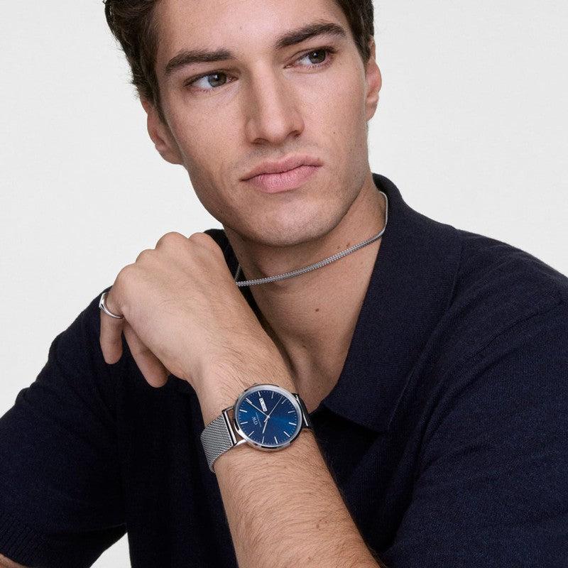 Daniel Wellington Classic Day Display watch featuring a blue dial and silver stainless steel mesh strap on a man's wrist.