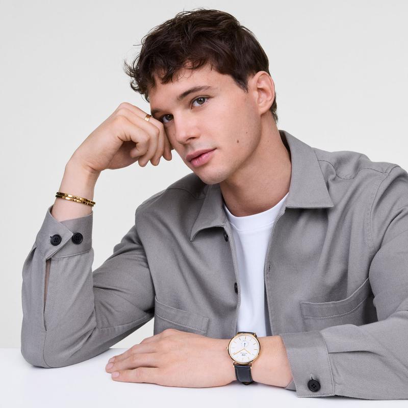 Daniel Wellington 40mm gold watch with off-white sunray dial and black leather strap on a man's wrist.