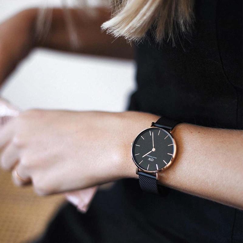Daniel Wellington Petite Ashfield 32mm watch with a black dial and rose gold case on a matte black mesh strap.