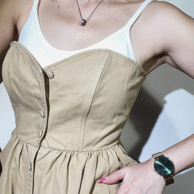 Daniel Wellington Petite Emerald watch with a dark green sunray dial and polished gold mesh strap on a wrist.